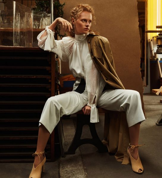 Frau sitzt elegant gekleidet auf Stuhl neben Tresen, trägt tolles Hair & Make-up