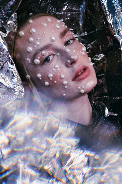 Junge, sommersprossige Frau zwischen Alufolie mit Perlen Make-Up & Glitter