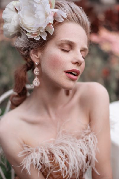 Junge, hellhäutige Frau in historischem Make-up Look, Blumenhaarschmuck, Federkleid, Perlenohrringe